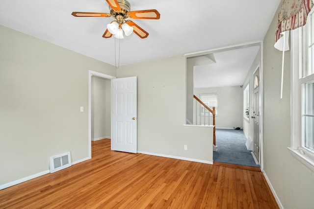 empty room featuring light wood-style flooring, stairs, visible vents, and baseboards