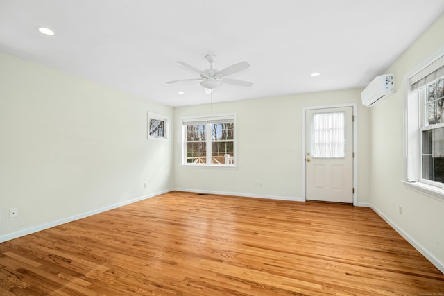 unfurnished room with a wealth of natural light, an AC wall unit, light wood-style flooring, and baseboards