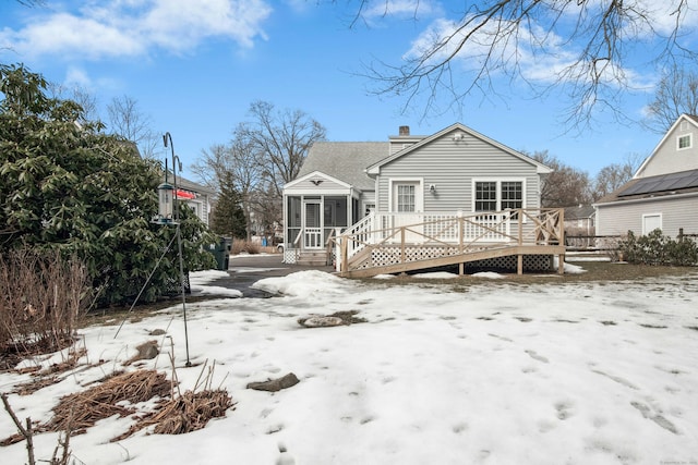 snow covered house featuring a chimney, a sunroom, and a deck