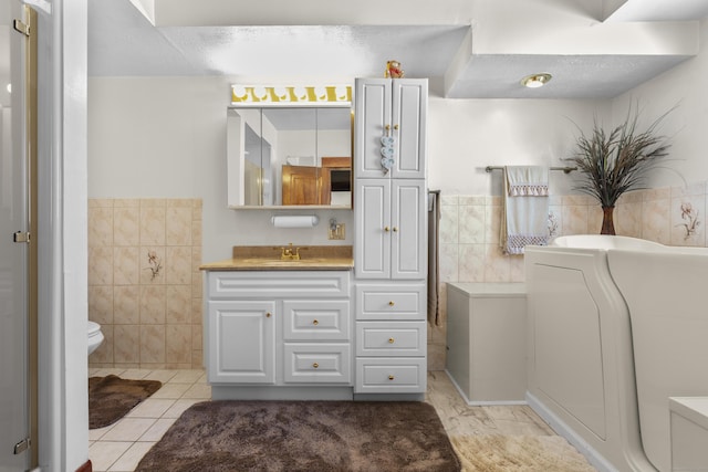 bathroom with tile walls, toilet, vanity, a tub, and tile patterned flooring