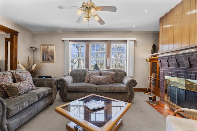 carpeted living room with ceiling fan, a fireplace, baseboards, and crown molding