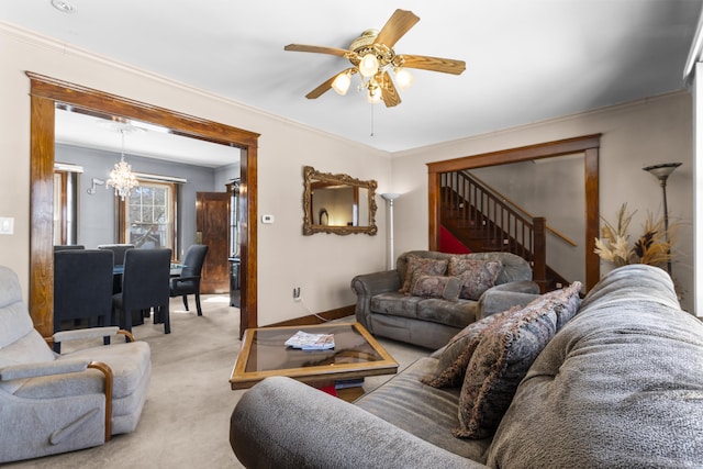 living area with ceiling fan with notable chandelier, carpet floors, stairs, and crown molding