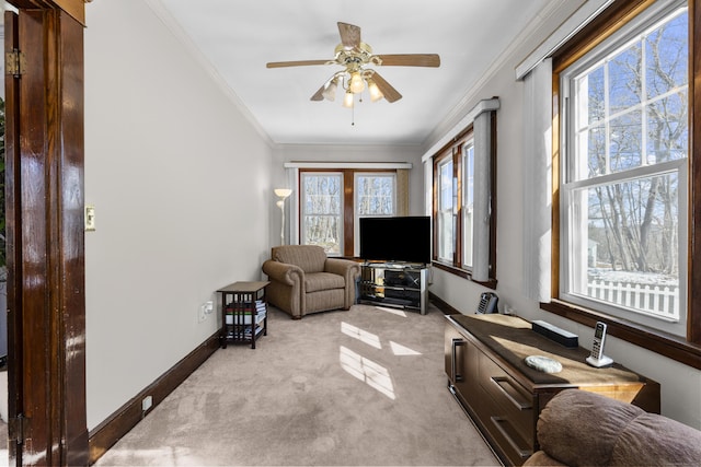 living area with light carpet, ceiling fan, baseboards, and crown molding