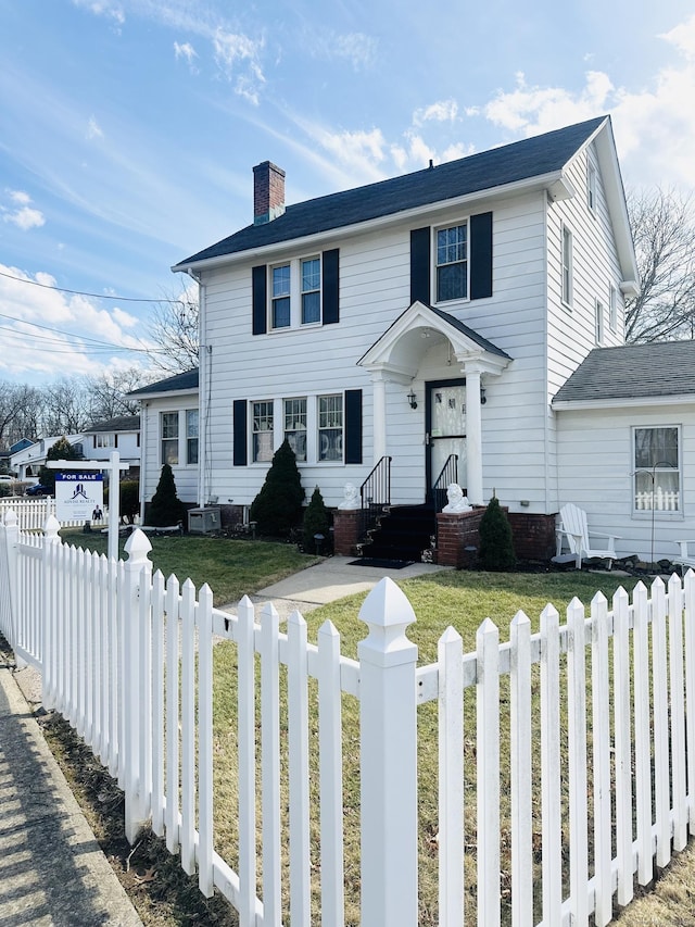 colonial home featuring a fenced front yard, a chimney, and a front lawn