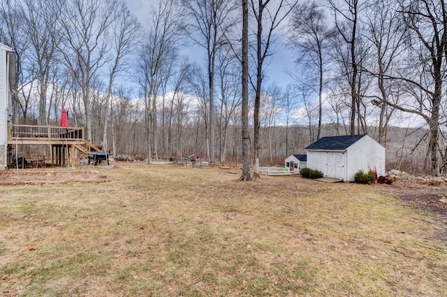 view of yard with a storage shed, an outdoor structure, a forest view, and a wooden deck