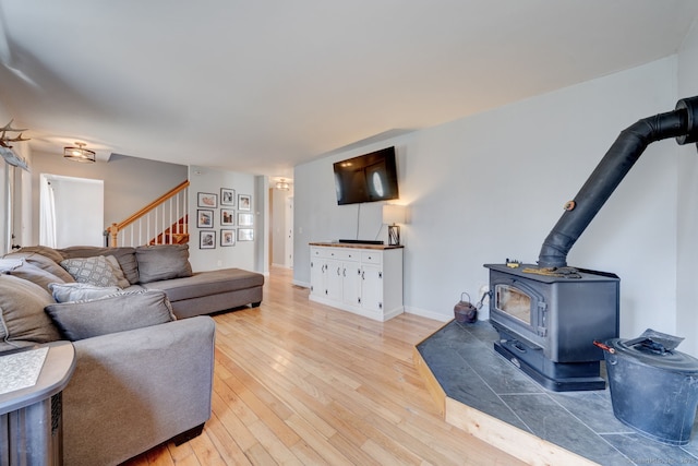 living area with baseboards, stairs, a wood stove, and light wood-style floors