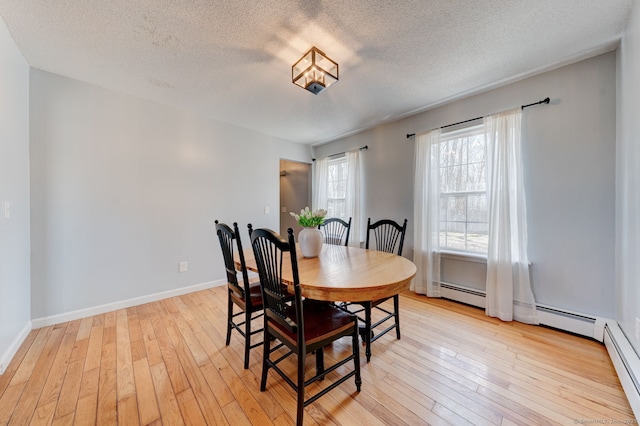 dining space featuring a baseboard heating unit, baseboards, light wood-type flooring, and a textured ceiling