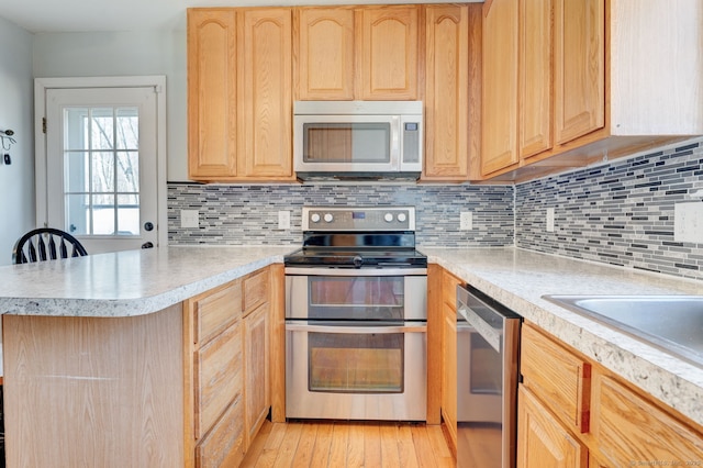 kitchen featuring light countertops, a peninsula, appliances with stainless steel finishes, and light brown cabinetry