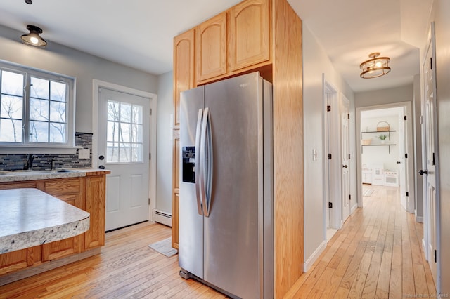 kitchen with light brown cabinets, baseboard heating, light wood-style flooring, stainless steel fridge, and a sink