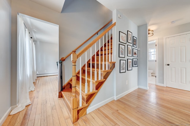 staircase with a baseboard heating unit, baseboards, and hardwood / wood-style floors