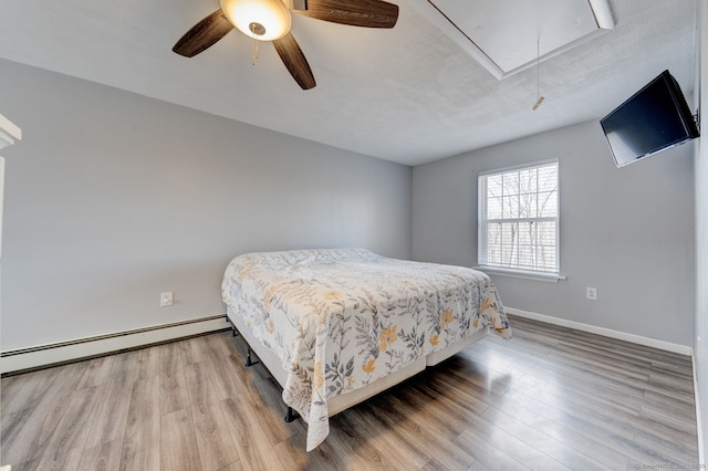 bedroom with a baseboard heating unit, attic access, wood finished floors, and baseboards