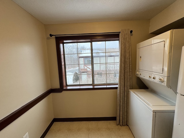 clothes washing area featuring a textured ceiling, laundry area, stacked washing maching and dryer, and baseboards