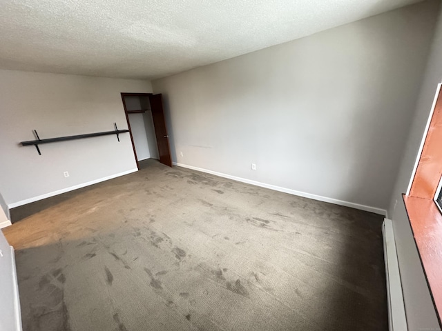 empty room featuring a textured ceiling, baseboard heating, dark carpet, and baseboards