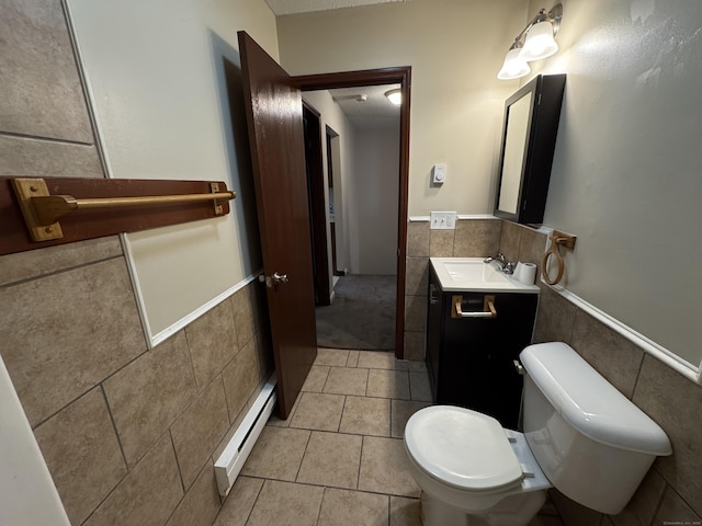 half bath with a wainscoted wall, a baseboard radiator, tile patterned flooring, vanity, and tile walls