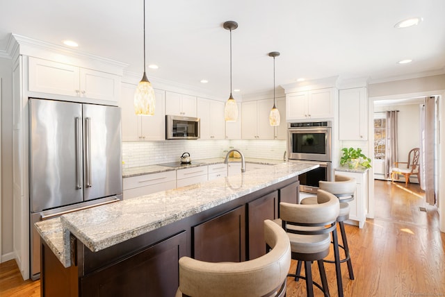 kitchen with hanging light fixtures, a kitchen island with sink, appliances with stainless steel finishes, and white cabinets