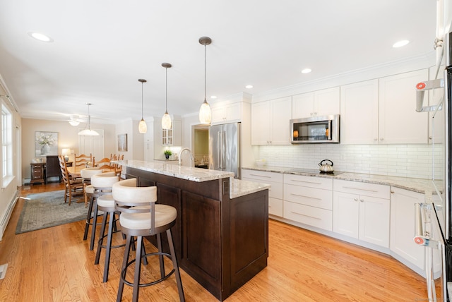 kitchen with white cabinetry, appliances with stainless steel finishes, light stone countertops, a center island with sink, and pendant lighting