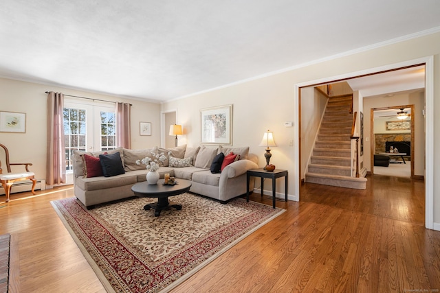 living room with stairs, ornamental molding, wood finished floors, and a stone fireplace