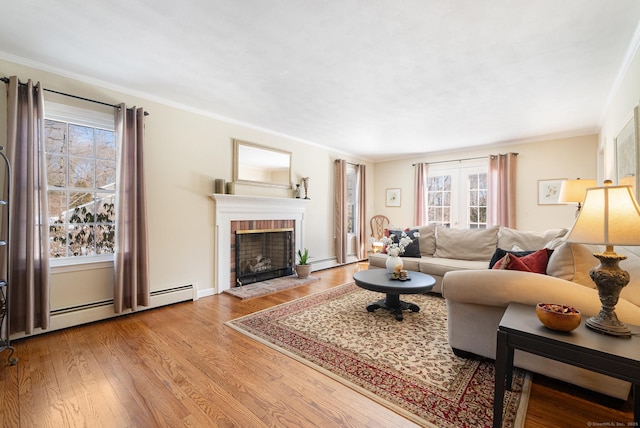 living area featuring crown molding, a baseboard heating unit, a fireplace, and light wood-style floors