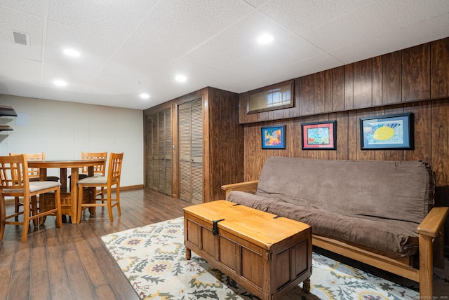 living room with wooden walls, visible vents, a drop ceiling, and wood finished floors