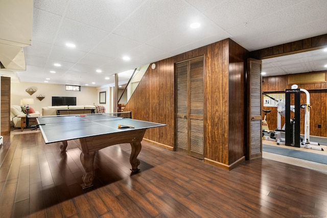 rec room with dark wood-type flooring, a paneled ceiling, and wooden walls