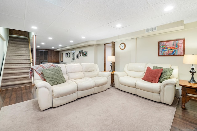 living room with a drop ceiling, recessed lighting, wood finished floors, visible vents, and stairway