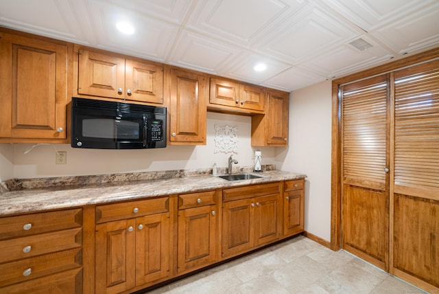 kitchen featuring visible vents, black microwave, brown cabinetry, and a sink