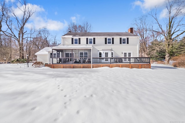 snow covered rear of property with a deck and a chimney