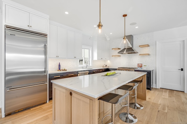 kitchen with tasteful backsplash, appliances with stainless steel finishes, wall chimney range hood, and light wood-type flooring