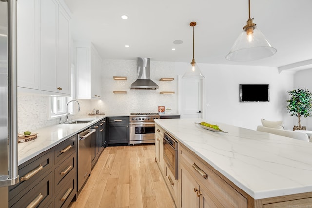 kitchen with light wood finished floors, wall chimney exhaust hood, a kitchen island, stainless steel appliances, and a sink