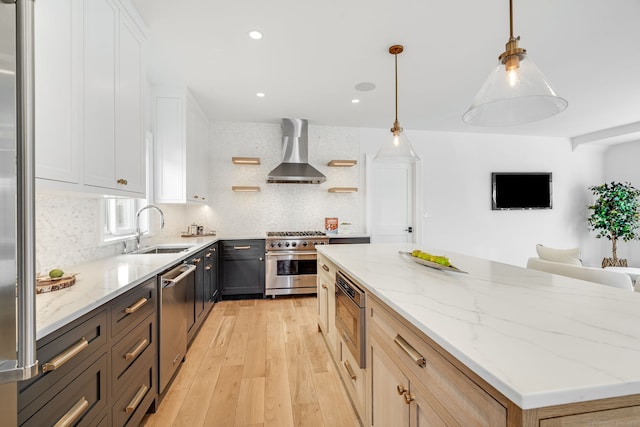 kitchen featuring appliances with stainless steel finishes, a kitchen island, light wood finished floors, a sink, and wall chimney exhaust hood