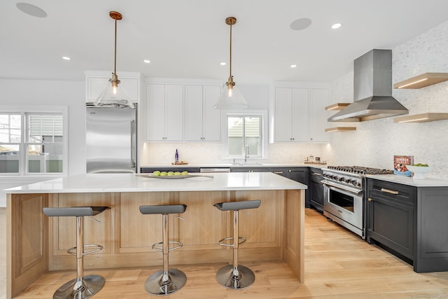 kitchen featuring a breakfast bar, wall chimney exhaust hood, high quality appliances, and white cabinets