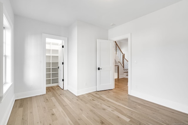 unfurnished bedroom featuring light wood-style floors, baseboards, a walk in closet, and a closet