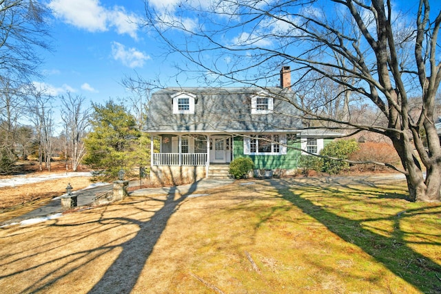 view of front of property featuring a porch, a shingled roof, driveway, a chimney, and a front yard