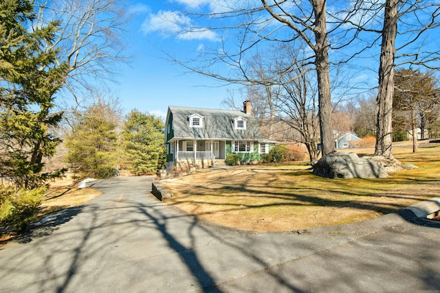 dutch colonial featuring a chimney, a front lawn, and a porch