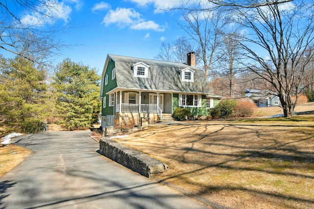 colonial inspired home featuring covered porch, a shingled roof, a chimney, and a gambrel roof