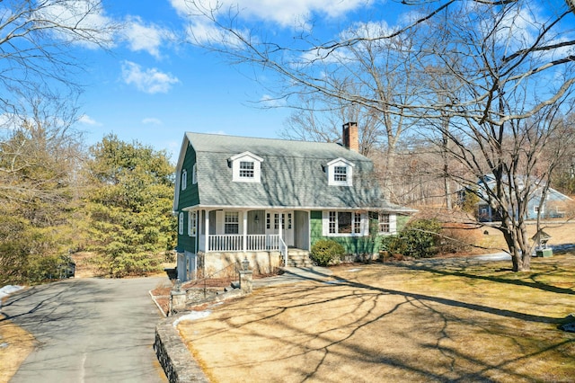 dutch colonial with covered porch, driveway, a shingled roof, and a chimney