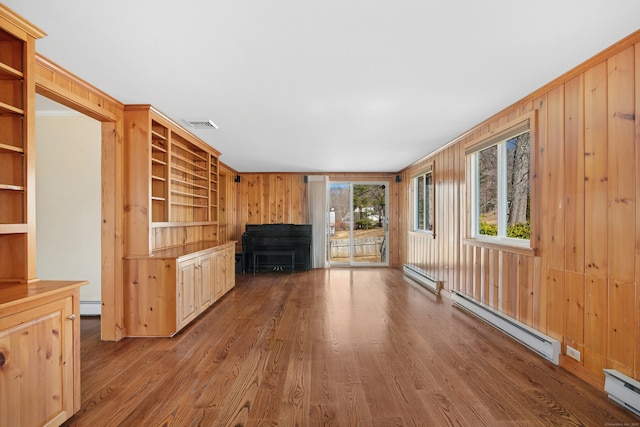 unfurnished living room featuring a baseboard heating unit, a baseboard radiator, wood walls, and wood finished floors