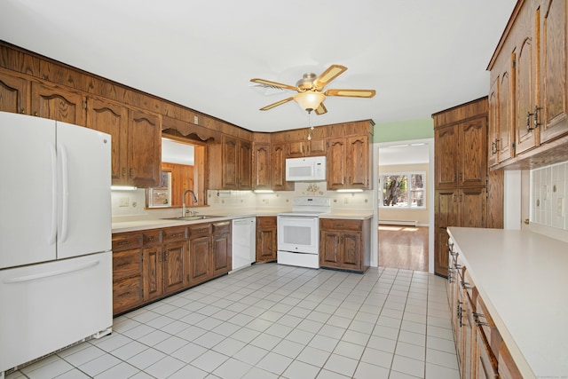 kitchen featuring brown cabinets, white appliances, light countertops, and a sink