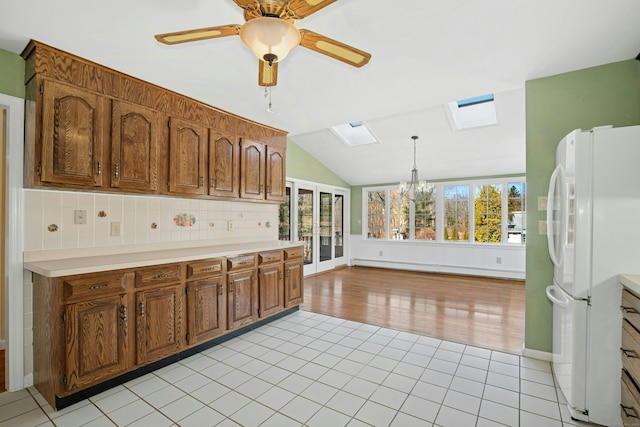 kitchen featuring light tile patterned flooring, a baseboard radiator, light countertops, freestanding refrigerator, and brown cabinetry