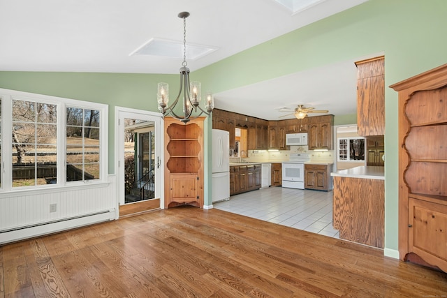 kitchen with a baseboard heating unit, white appliances, light wood-style floors, light countertops, and lofted ceiling with skylight