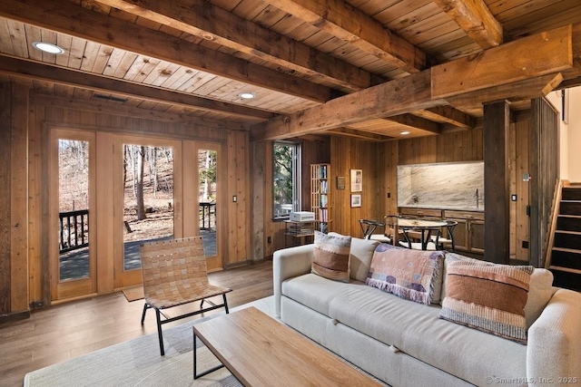 living room with stairway, light wood-style flooring, wood walls, wooden ceiling, and beamed ceiling