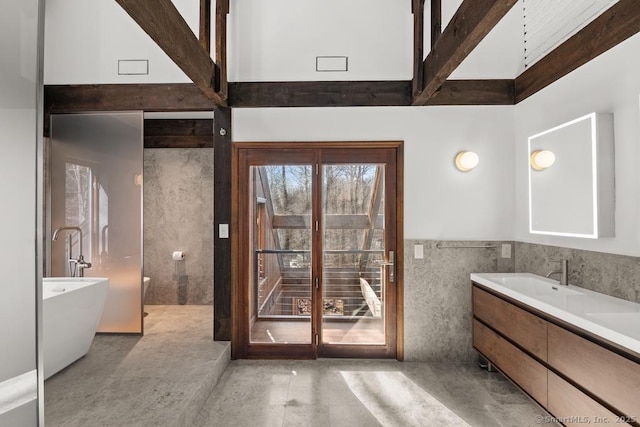 bathroom with a soaking tub, vanity, a towering ceiling, and tile walls