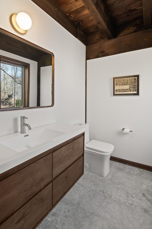 half bath featuring wooden ceiling, toilet, vanity, baseboards, and beam ceiling