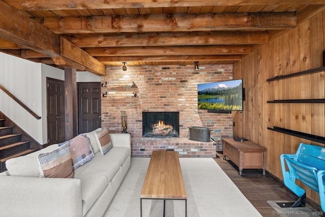 living area with beam ceiling, stairway, a brick fireplace, wooden walls, and wood finished floors