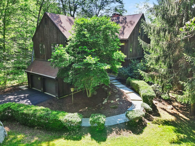 view of home's exterior with aphalt driveway, a shingled roof, a chimney, and an attached garage