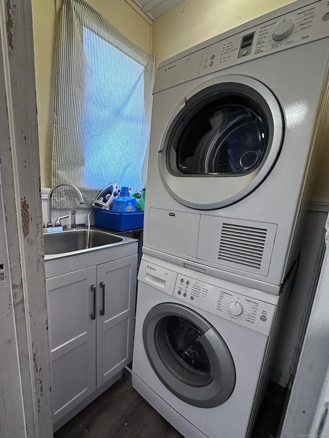 laundry area featuring dark wood-type flooring, stacked washer / dryer, laundry area, and a sink