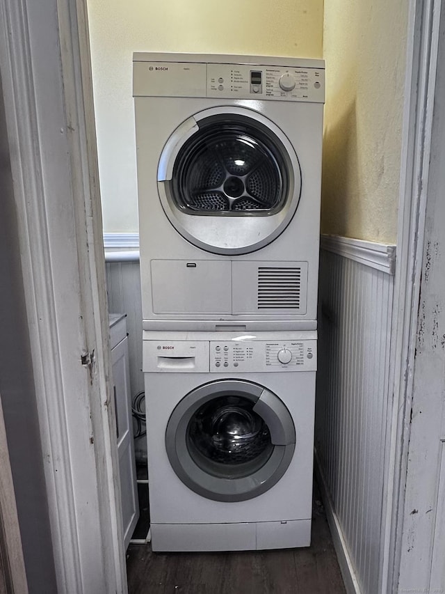 washroom featuring laundry area, wainscoting, stacked washing maching and dryer, and dark wood finished floors