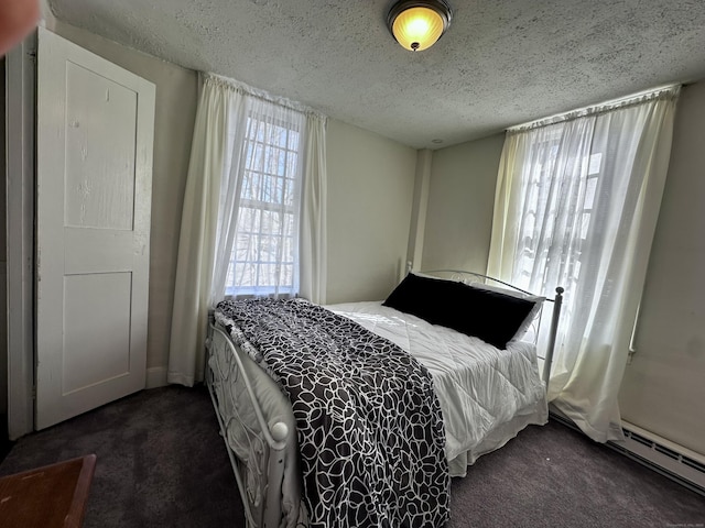 bedroom with a baseboard heating unit, a textured ceiling, and dark carpet