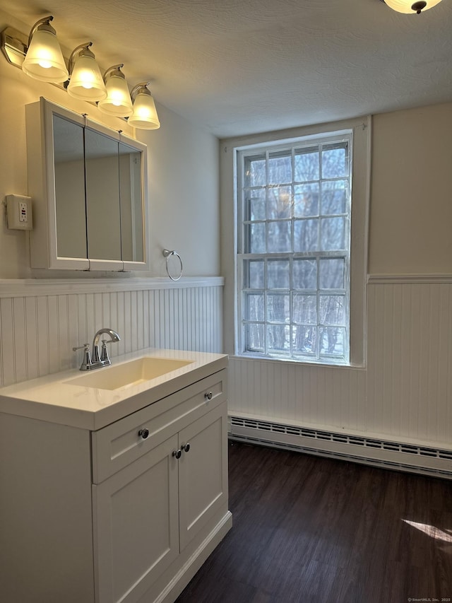 bathroom with vanity, a baseboard heating unit, wood finished floors, and wainscoting