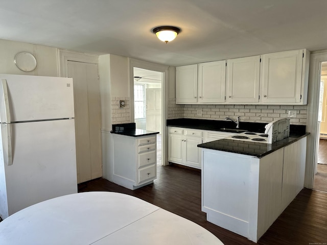 kitchen with dark wood-style floors, dark countertops, freestanding refrigerator, white cabinets, and a peninsula